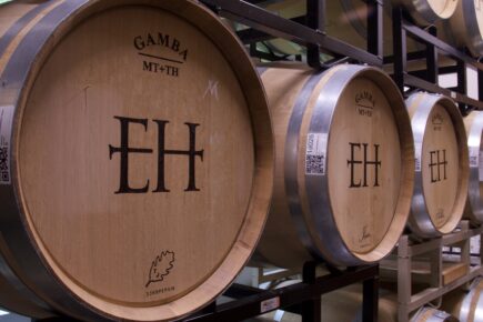 Close-up of wine barrels at Eagle Harbor Wine Company, featuring the company's logo 'EH' prominently engraved on the front. The barrels are arranged on racks, displaying the craftsmanship of the oak wood with metal hoops and branding details.