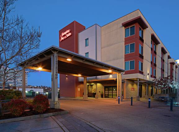 Exterior of Hampton Inn & Suites Bremerton on the waterfront at dusk, showing hotel entrance and covered drop-off area in downtown Bremerton, Washington.