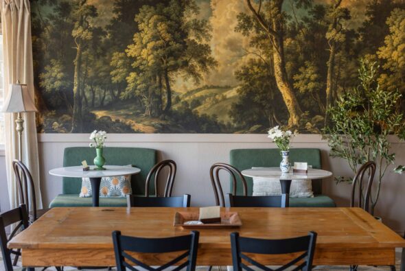 Cozy dining nook at Old Town Kitchen in Silverdale, WA, with a wraparound forest mural, green banquette seating, round marble bistro tables, and fresh white flowers.