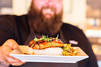 photo of bearded man holding dish of food at Axe and Arrow Gastropub