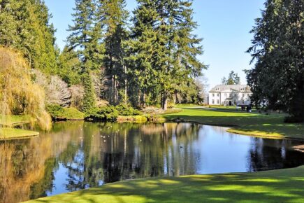 Reflection pond and manicured lawns at Bloedel Reserve on Bainbridge Island, with tall evergreen trees and the historic Bloedel estate home in the background.