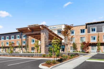 Exterior photo of the Fairfield Inn & Suites Seattle in Poulsbo, WA. There are clear blue skies above the hotel and an empty parking lot in front of the hotel.