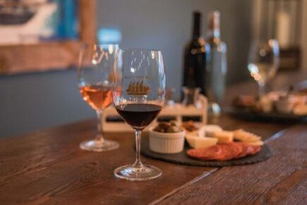 A cozy setting at Fletcher Bay Winery featuring glasses of red and rosé wine on a wooden table, accompanied by a charcuterie board with cheese, cured meats, and olives. The relaxed atmosphere reflects a perfect pairing experience, with wine bottles in the background adding to the intimate ambiance.