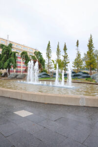 Water fountains spouting from the ground at Harborside Fountain Park in Bremerton, WA, surrounded by trees and nearby buildings.