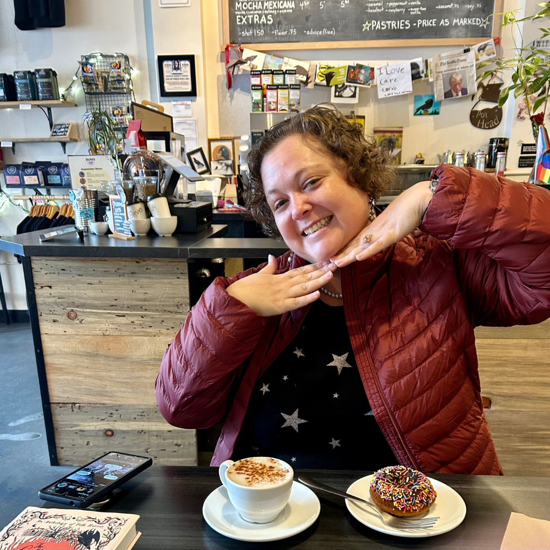 Jess Senires enjoying a coffee break at Cafe Corvo in Bremerton, WA, during her 3-day staycation. Her cheerful pose perfectly matches the vibrant atmosphere of the cafe.