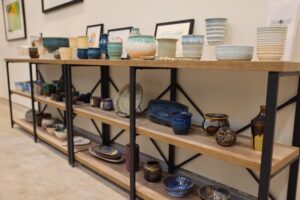 Wooden shelves displaying various handcrafted pottery pieces, including bowls, vases, and cups. The ceramic items are arranged neatly, showcasing different colors and glazes.