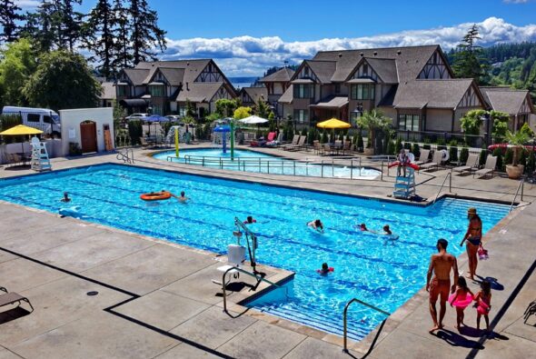 Guests enjoying the outdoor pool at The Inn at Pleasant Beach in Bainbridge Island, surrounded by village-style buildings and evergreen hills.