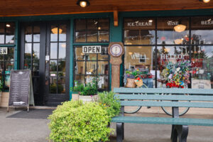 The front of the historic Port Gamble General Store with “OPEN” signs, vintage decor, flowers, and a green bench.