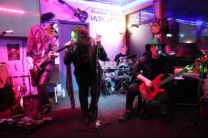 Live rock band playing at Brother Don’s in Bremerton, featuring a vocalist, guitarist, bassist, and drummer under colorful stage lights.