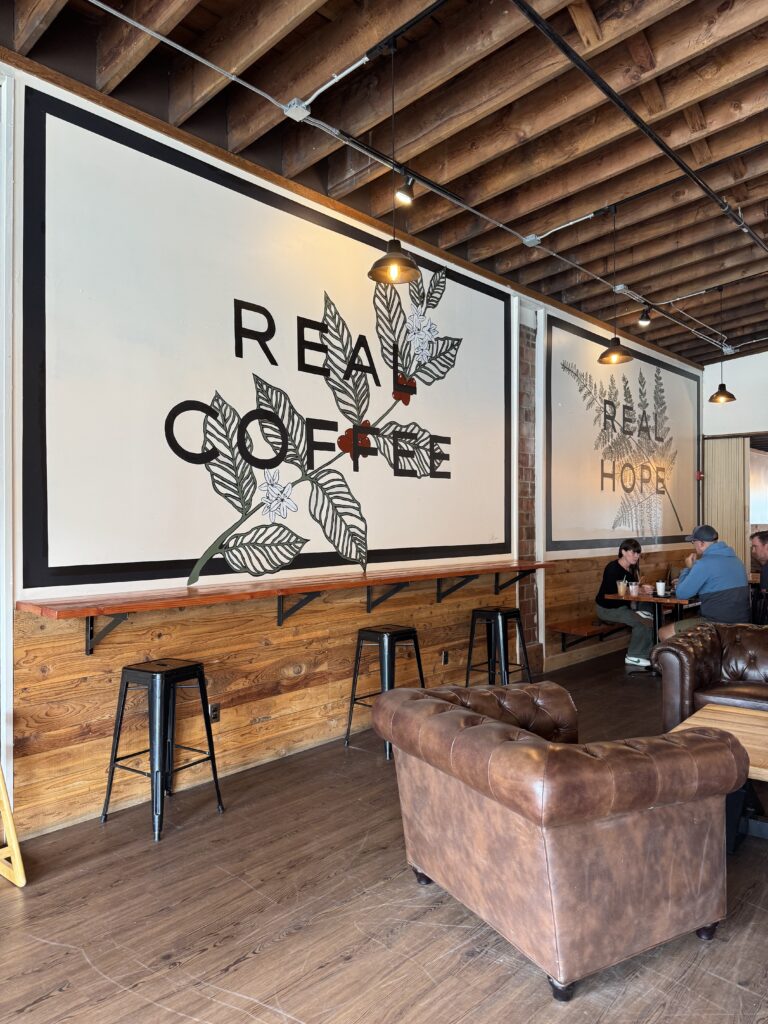 Cozy coffee shop interior at Coffee Oasis in Bremerton, featuring leather couches, wood walls, and wall art reading “REAL COFFEE” and “REAL HOPE.”