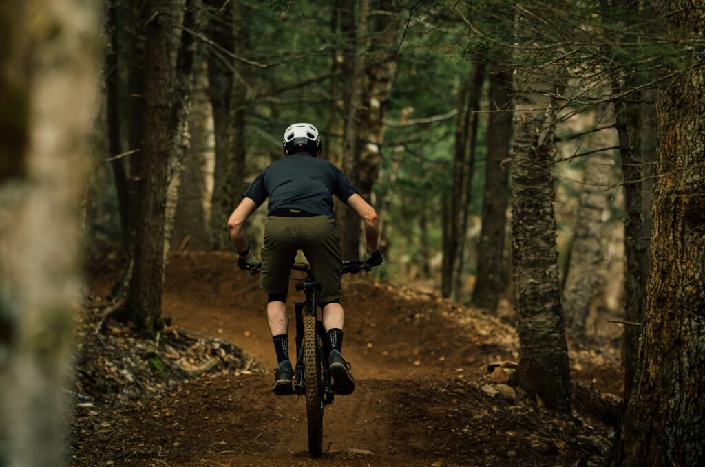 Man mountain biking through a forest trail at Port Gamble Heritage Park on the Kitsap Peninsula, surrounded by tall trees and autumn leaves.