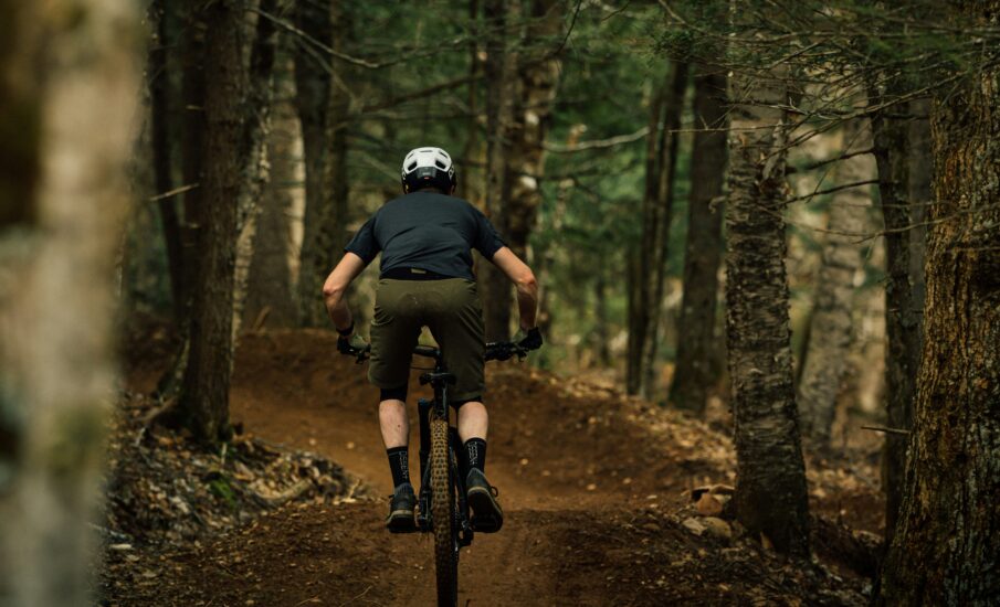 Man mountain biking through a forest trail at Port Gamble Heritage Park on the Kitsap Peninsula, surrounded by tall trees and autumn leaves.